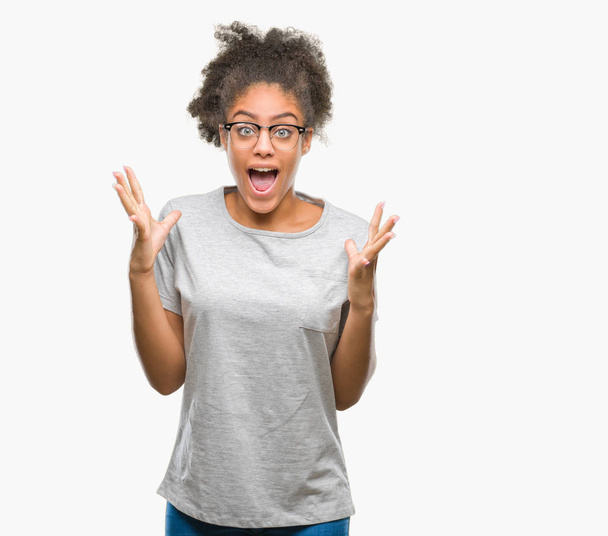 Young afro american woman wearing glasses over isolated background celebrating crazy and amazed for success with arms raised and open eyes screaming excited. Winner concept - Foto, imagen