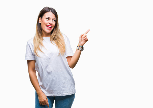 Giovane bella donna casual bianco t-shirt su sfondo isolato con un grande sorriso sul viso, puntando con mano e dito verso il lato guardando la fotocamera
. - Foto, immagini
