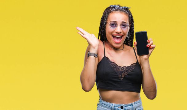 Young braided hair african american with birth mark showing smartphone screen over isolated background very happy and excited, winner expression celebrating victory screaming with big smile and raised hands - Foto, afbeelding