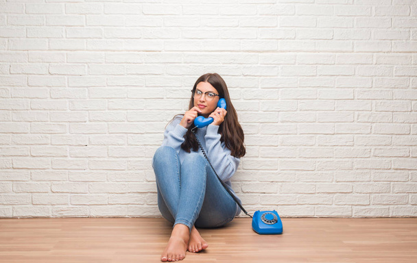 Jeune femme brune assise sur le sol faisant appel à un téléphone vintage visage sérieux réfléchissant à la question, idée très confuse
 - Photo, image