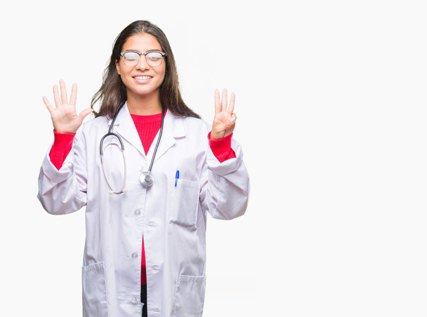Молодая арабская доктор женщина на изолированном фоне показывает и указывает пальцами номер восемь, улыбаясь уверенно и счастливо
. - Фото, изображение