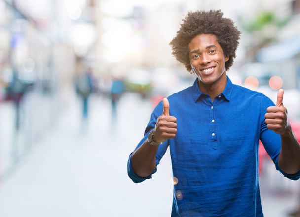 Afro americký muž nad izolované pozadí úspěch znamení dělá pozitivní gesto rukou, palec se usmívá a šťastný. Při pohledu na fotoaparát s veselým výrazem, vítěz gesto. - Fotografie, Obrázek