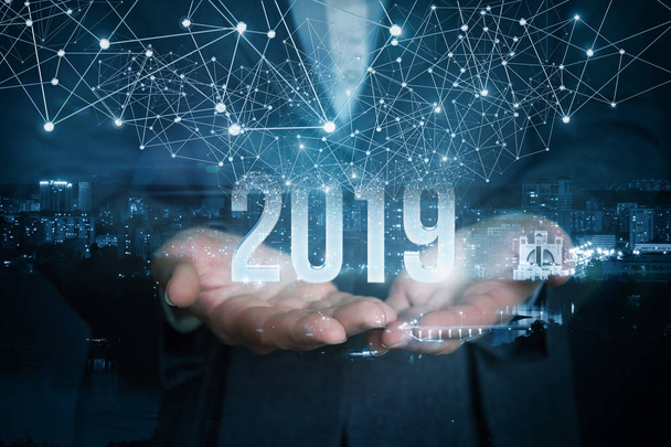 A businesswoman is holding the 2019 year numbers inside the night city image picture with distinct wireless connections above. - Photo, Image
