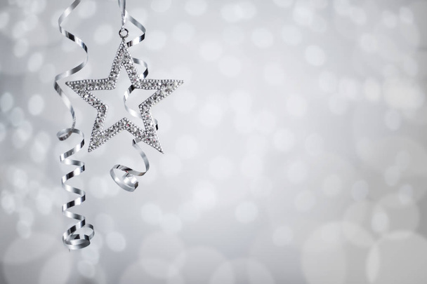 Zilveren Kerst Nieuwjaar krullend streamer lint en ster over reflecterende achtergrond van de lichten van de bokeh met kopie ruimte voor tekst - Foto, afbeelding