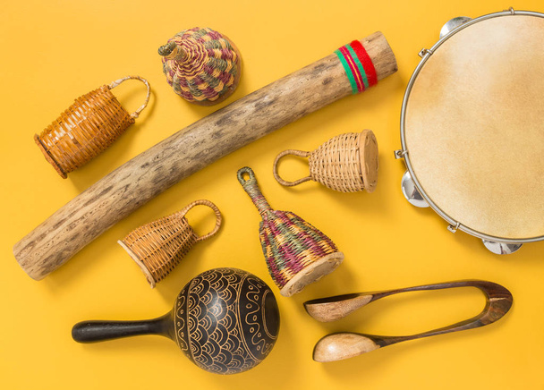Strumenti musicali a percussione etnica su sfondo giallo. Caxixi shaker, rainstick, pandeiro, maracas e cucchiai musicali
.  - Foto, immagini