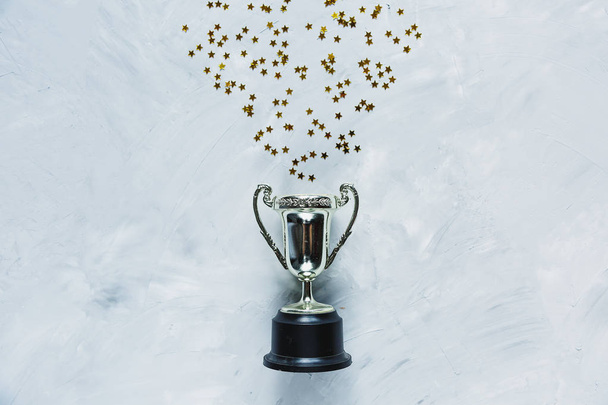 Kultainen pokaali ja tähdet konfetti harmaalla sementillä taustalla. urheilun saavutus, menestyksen käsite. Kultainen pokaali johtajana. Yrityksen menestys
. - Valokuva, kuva