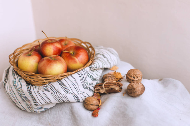 Stillleben mit Äpfeln in einem Weidenkorb stehen auf einem gestreiften Leinenstoff, Walnüsse, Blütenblätter und Zimtstangen in Bindfäden gewickelt. Dankeschön-Karte für Herbst- und Herbstkonzepte. - Foto, Bild