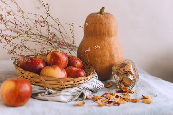 Still life with cinnamon sticks wrapped in twine, apples in a wicker basket stand on a striped linen cloth, walnuts and flower petals. Concept of home comfort in autumn or winter. - Фото, зображення