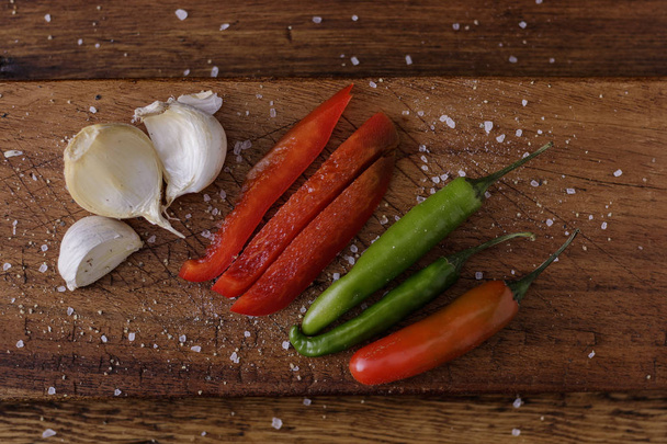 Česnek a chilli papričky na dřevěné desce s přídavkem koření k vaření a ochucení potravin - Fotografie, Obrázek