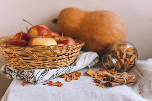 Still life with cinnamon sticks wrapped in twine, apples in a wicker basket stand on a striped linen cloth, walnuts and flower petals. Concept of home comfort in autumn or winter. - Fotografie, Obrázek