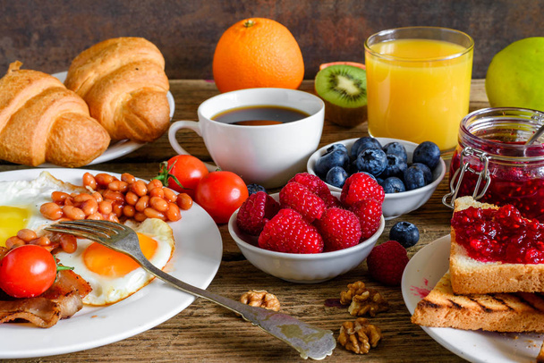 Англійський сніданок - смажені яйце, квасоля, помідори, кава, бекон і тости з апельсинового соку, свіжі фрукти і ягоди з виделкою. крупним планом - Фото, зображення