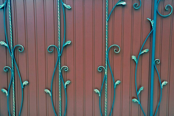 Een fragment van rode ijzeren deuren met smeedijzeren staven en een prachtig patroon - Foto, afbeelding