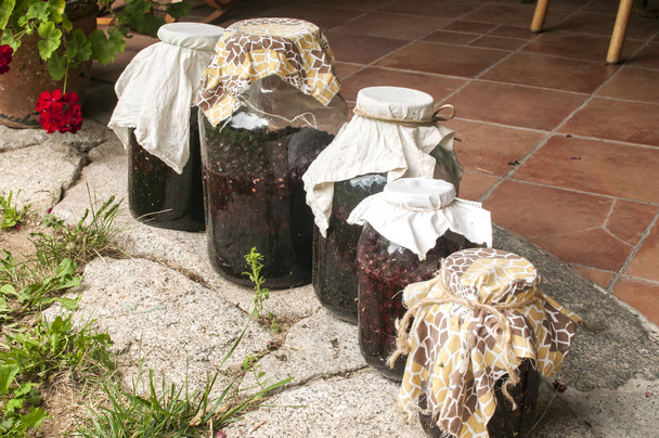 Frascos de vidro grandes com cerejas azedas embebidas em açúcar e fermentação em álcool para fazer closeup de licor caseiro no quintal da casa
 - Foto, Imagem