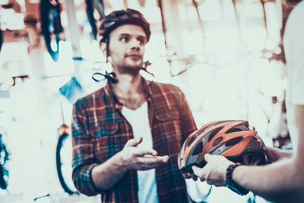 Konsultant pomoże facet wybrać kask do przejażdżek rowerowych. Portret kaukaski klient sobie czerwone kraciaste koszule, pomiar różnych nowoczesne hełmy w Sport sklep rowerowy z niewyraźne tło - Zdjęcie, obraz