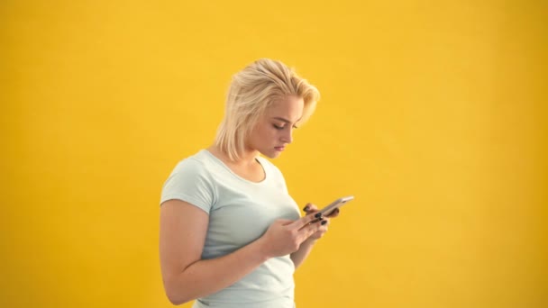 Unhappy blond plus size model surprised checking message on phone at yellow background - Metraje, vídeo