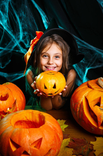 Vrolijke Halloween. Schattig klein kind meisje in heks kostuum met snijwerk pompoen. Voorbereiden van Halloween en gelukkige familie. - Foto, afbeelding