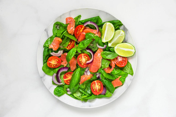 Ispanak, cherry domates, kırmızı soğan, limon ve beyaz mermer zemin üzerine bir tabak içinde fesleğen somon salatası. sağlıklı gıda kavramı. üstten görünüm - Fotoğraf, Görsel