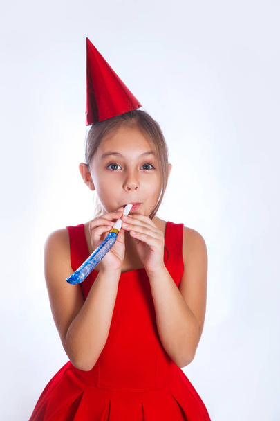 Little smiling girl with birthday hat and whistle on white background. Celebration and party - 写真・画像