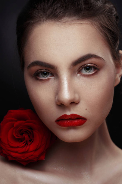 Beauty fashion portrait of an elegant sexy girl with a red rose on her shoulder on a black background. - Foto, afbeelding