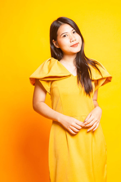 Beautiful young Asian woman in yellow dress on yellow background - 写真・画像