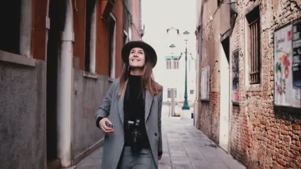Attractive happy professional female photographer walking with camera smiling along beautiful old street in Venice Italy - Materiał filmowy, wideo