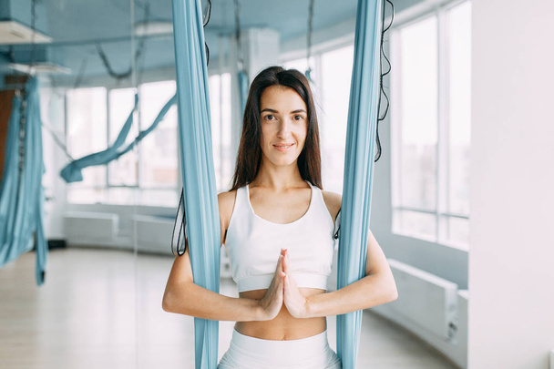 Beautiful girl sitting and smiling in training. Relax and unwind on the yoga hammock.  - Foto, Imagem