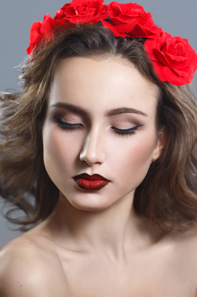 Beauty portrait of a beautiful woman with red lipstick and a decorative wreath on a gray background. - Photo, image