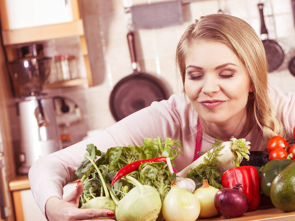 Funny joyful young woman, cooking chef having many healthy vegetables on table. Tomatoes, onion, lettuce, pepper. Vegetarian lifestyle concept. - 写真・画像