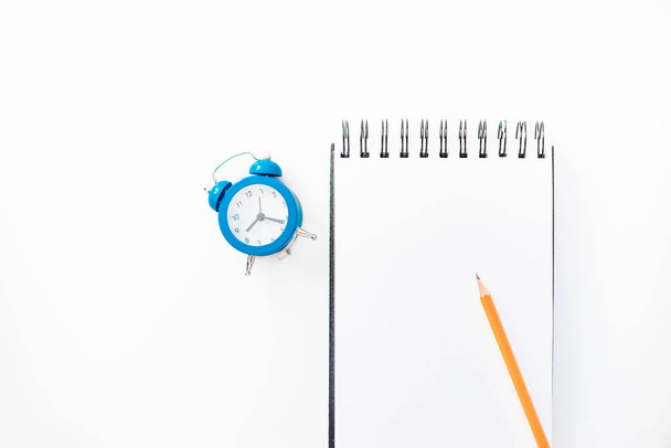 Λευκό σκίτσο βιβλίο με μολύβι πορτοκαλί και μπλε ρολόι συναγερμών. Εκπαίδευση και την ιδέα του σχεδιασμού, αφηρημένα φόντο λευκό. Μακέτα έννοια. Λευκό φόντο, απομονωμένες, κοντινό πλάνο  - Φωτογραφία, εικόνα