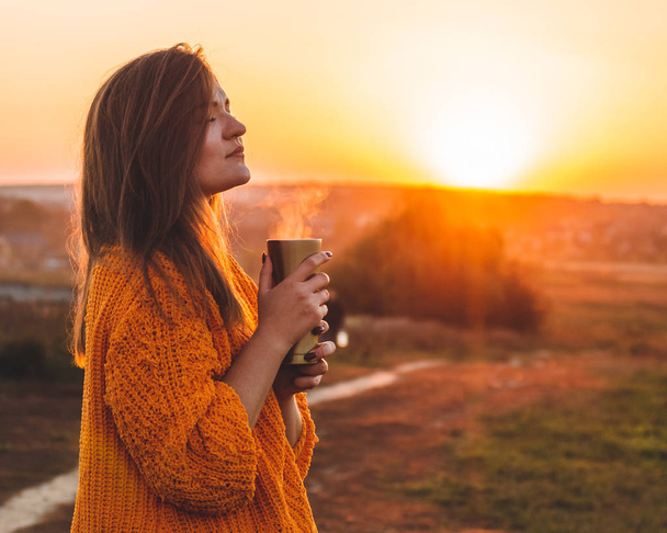 Fiatal nő egy narancssárga pulóver termosz thermo csésze puha napsütéses nyári szabadtéri portré. Ősszel. Naplemente. A hangulatos - Fotó, kép
