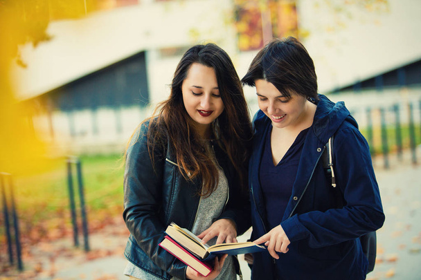 大学キャンパスにおける屋外一緒に本を読んで 2 つの笑みを浮かべて女子校生.  - 写真・画像