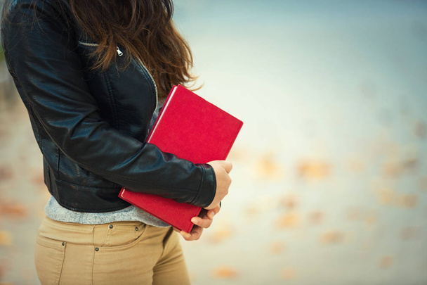 Close up of student girl body holding a red book, education concept. Outdoors lifestyle view with copy space. - Φωτογραφία, εικόνα