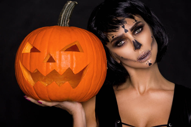 Sexy morena en maquillaje y lencería de Halloween sostiene una calabaza sobre un fondo negro en el estudio. Maquillaje esqueleto, monstruo y bruja
 - Foto, Imagen