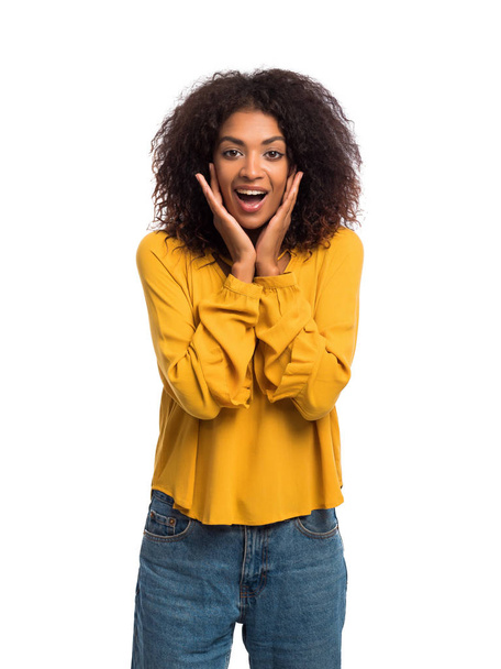 Beautiful african american woman with afro hair in yellow wear smiling, pleasantly surprised to camera over white wall background. Cute mixed race girl's portrait with amazement - Photo, image