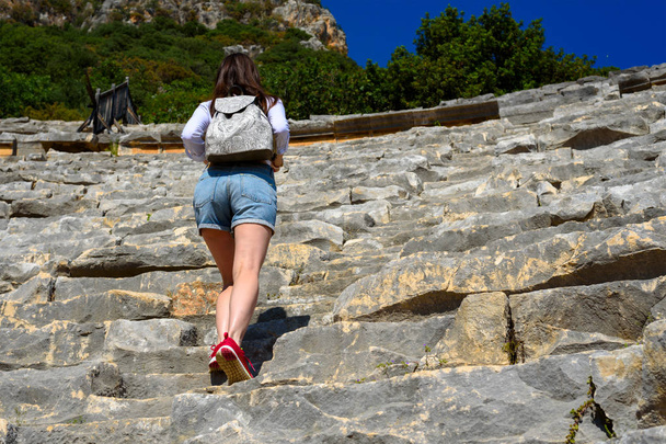 молодая женщина в джинсовых шортах и рюкзаке прогуливается по руинам амфитеатра, прикосновение к истории, путешествие, перемещение вверх, скопировать пространство
 - Фото, изображение