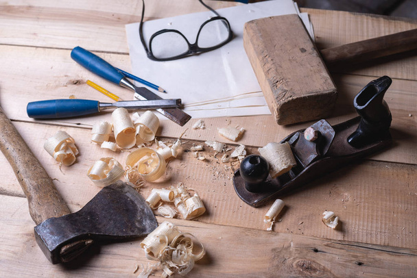 Плотник инструментов на деревянном столе с опилками, плантатором, молотком, топором, зубилом, очками
 - Фото, изображение