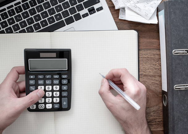 vista superior del hombre utilizando la calculadora en el escritorio con la carpeta, recibos o facturas y portátil
 - Foto, imagen