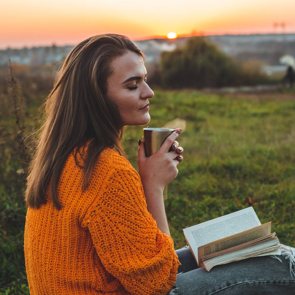 das Konzept der Lifestyle-Outdoor-Erholung im Herbst. Mädchen las Bücher auf Plaid mit einem Thermobecher. Herbst. Sonnenuntergang. gemütlich - Foto, Bild