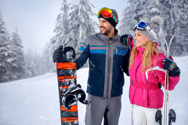 smiling young couple skiing and snowboarding enjoying in snowy mountains together - Zdjęcie, obraz