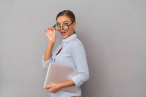 Image of surprised happy business young woman posing isolated over grey wall background holding laptop computer. - Foto, Bild