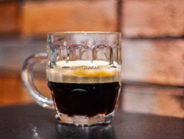 Close up on a glass of dark beer on wooden table in bar on brick wall background - Valokuva, kuva