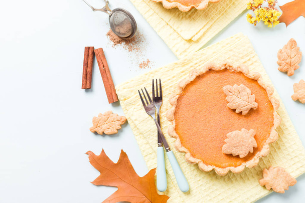 Pompoen taart met kaneel en cookies op gele servetten op pastel blauwe achtergrond met bladeren van de herfst geel - bovenaanzicht close-up fotografie van seizoensgebonden Amerikaanse traditionele zoete gebakken voedsel. - Foto, afbeelding