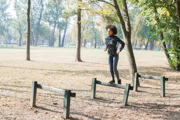 秋の公園、実行して、ハードルを飛び越えての朝フォレストのアフリカ女性のトレーニング. - 写真・画像