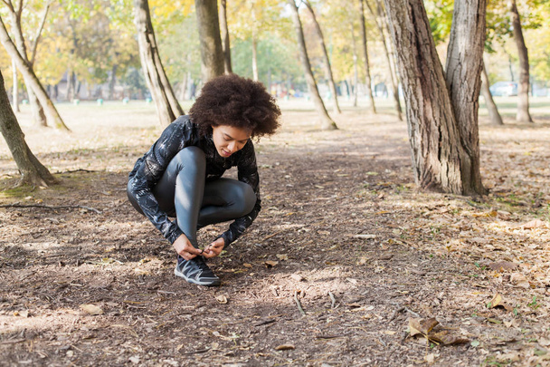 Спортивна жінка готова або розслабляється для бігу в лісі, жінка бігунка зав'язує шнурки взуття після тренування
. - Фото, зображення
