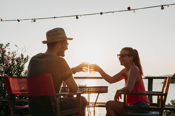 Couple enjoying sunset in a beach bar drinking beer - Фото, изображение