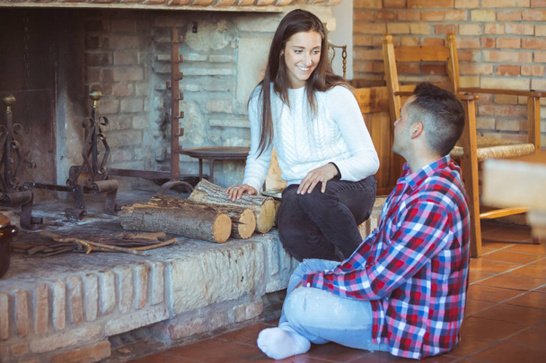 Young shy people (man and woman) met at friends party - young couple talking near the fireplace trying to kindle a fire - seduction and love, romantic date, winter holidays celebration concept - 写真・画像