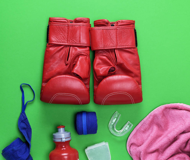 γάντια του μποξ κόκκινο δέρμα, ένα πλαστικό μπουκάλι νερού και μια πετσέτα ροζ και μπλε κλωστοϋφαντουργίας επίδεσμο σε πράσινο φόντο - Φωτογραφία, εικόνα