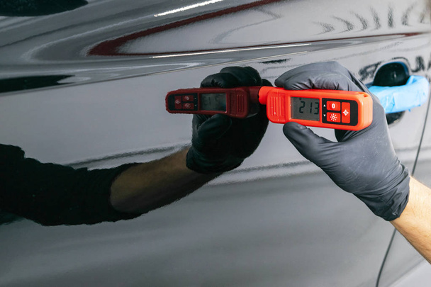 Male hand holds device for measuring coating thickness before polishing car. Measuring thickness of the car paint coating with paint thickness gauge. Polish car concept - 写真・画像
