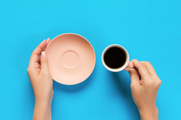 hohe Winkel der Frauenhände hält Kaffeetasse auf blauem Hintergrund minimalistischen Stil. flache Lage, von oben isoliert. - Foto, Bild