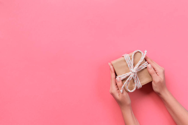 Женские руки с подарочной коробкой с розовой лентой на цветном фоне, вид сверху
. - Фото, изображение